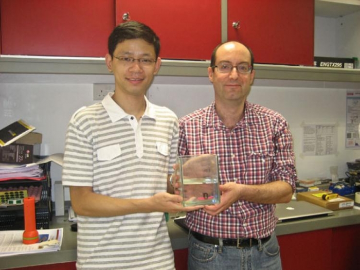 Dr. Baile Zhang (stanga), inventatorul dispozitivelor pe baza de calcit si Prof. George Barbastathis, parte din echipa de dezvoltare, tinand in mana dispozitivul intr-un rezervor cu "ulei de laser".