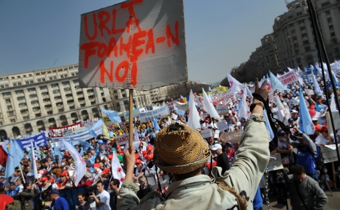 Un protestatar român face semnul victoriei în timp ce deţine o lectură pancartă "Urlă foamea-n noi" în timpul unui protest la Bucuresti, pe 16 martie 2011.