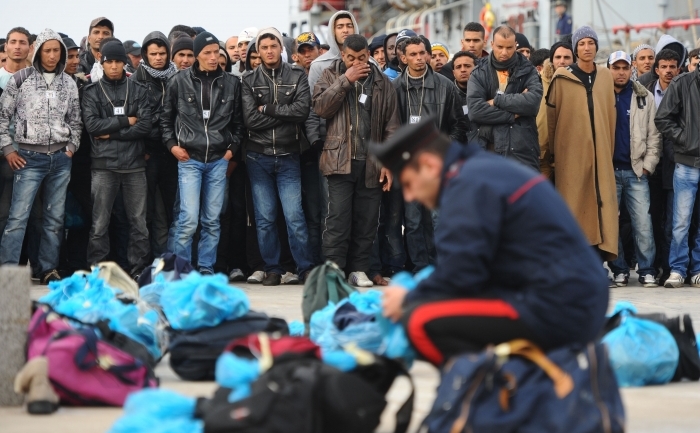 Poliţist verificând bunurile pe care le au asupra lor un grup de imigranţi, după ce au debarcat pe insula Lampedusa.