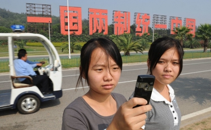 Turişti chinezi stau în faţa unui semn mare care spune, "O ţară, două sisteme, aceeasi China", o referire la China comunistă şi relaţia ambiguă democratica din Taiwan
