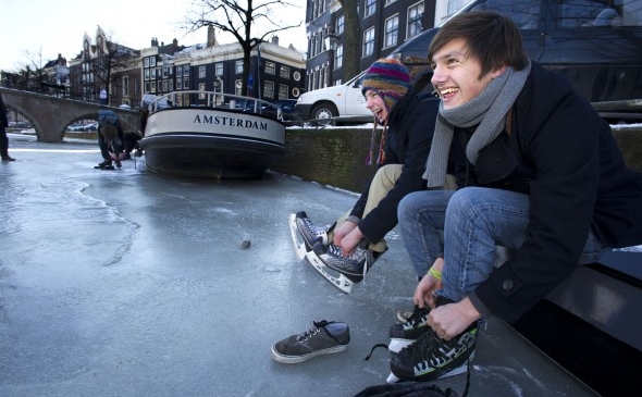 Tineri se pregătesc să patineze pe un canal îngheţat în Amsterdam, pe 6 februarie. Celebrul tur pe gheaţă naturală al celor 11 oraşe, nu va merge mai departe deoarece gheaţa este prea subţire pe alocuri (Evert Elzinga / AFP / Getty Images)