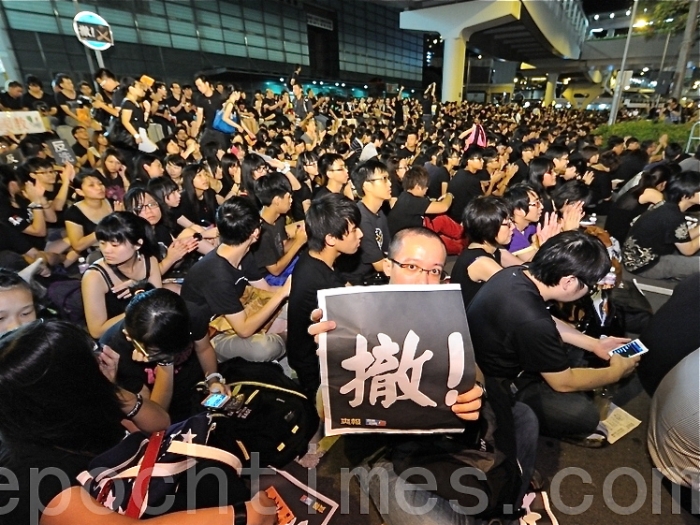 Mulţimi de oameni adunaţi lângă clădirea guvernului din Hong Kong, 7 septembrie 2012. Un protestatar ţine o pancardă pe care scrie "Înapoi"
