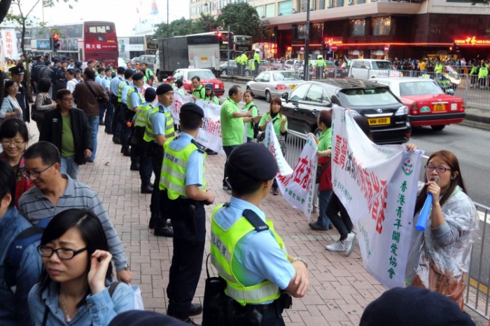 Activişti în uniforme verzi ţinând bannere anti-Falun Gong lângă un site de adunare a demisiilor din Partid al Epoch Times, Hong Kong