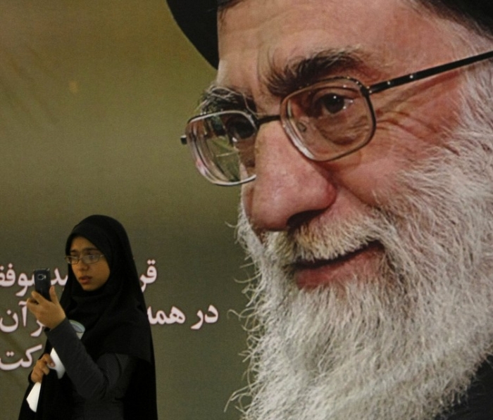 O femeie iraniană îşi verifică telefonul mobil în timp ce stă în faţa portretului liderului suprem al Iranului, Ayatollah-ul Ali Khamenei, în Teheran, 7 septembrie 2008.