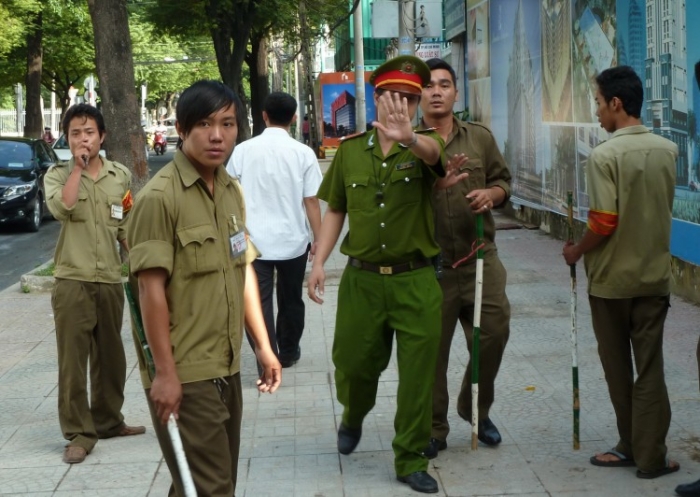 Un poliţist, flancat de membri ai unei miliţii locale, încearcă să oprească un jurnalist străin să facă poze în timp stau de pază în faţa Tribunalului Popular din Ho Chi Minh City, 10 august 2011, Vietnam.
