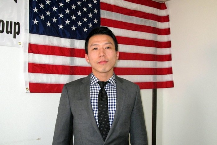 Kenny Hu stă în faţa steagul american. Hu lucrează acum cu normă întreagă pentru eliberarea tatălui său.
