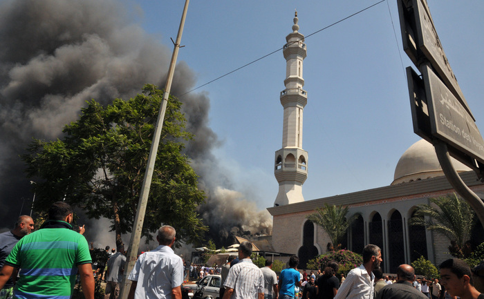 Se vede fumul deasupra oamenilor adunaţi în afara unei moschei la locul unei explozii puternice în nordul oraşului libanez Tripoli la 23 august 2013. Două explozii puternice au ucis mai multe persoane: una a zguduit centrul oraşului, lângă casa fostului premier Najib Mikati, al doilea a lovit în apropiere de portul oraşului agitat, cu o majoritate musulmană sunită. Exploziile vin la o saptamana dupa un atentat sinucigaş care a ucis 27 de persoane într-un bastion din Beirut deţinut de mişcarea şiită libaneză Hezbollah, care se luptă alături de forţele lui Assad. (IBRAHIM CHALHOUB / AFP / Getty Images)