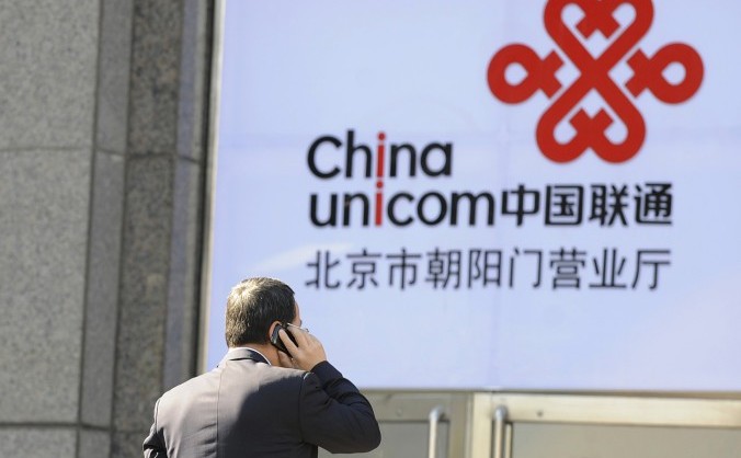 
Un bărbat vorbeşte la telefon în timp ce trece pe lângă logo-ul companiei chineze de telecomunicaţii China Unicom.