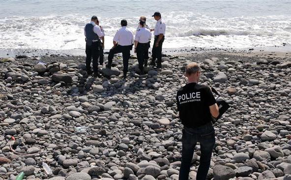 Ofiţeri de poliţie inspectează fragmentele metalice descoperite pe o plajă din Saint-Denis, pe insula franceză Reunion, în Oceanul Indian, 2 august 2015.