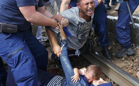 O familie de refugiaţi este săltată de poliţişti de pe o cale ferată din oraşul ungar Bicske, 3 septembrie 2015. (Captură foto)