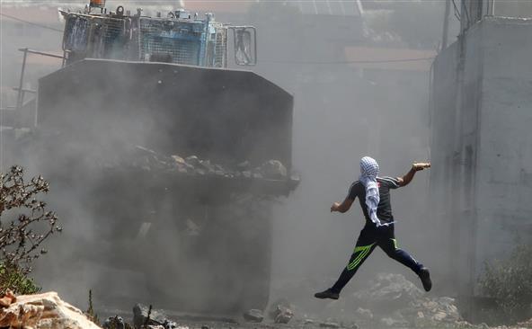 Un palestinian aruncă cu o sticlă plină cu vopsea asupra unui buldozer al armatei israeliene în timpul unor ciocniri între cele două tabere izbucnite după o demonstraţie împotriva confiscării pământurilor palestiniene de către Israel în satul Kafr Qaddum, în apropiere de Nablus, Cisiordania, 21 august 2015.