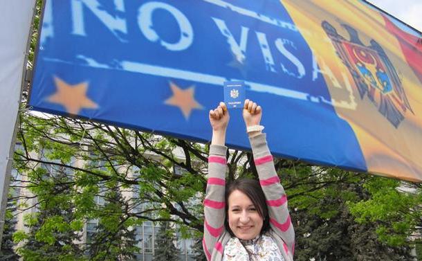O tânără stă cu un paşaport în mână în faţa unui steag al Republicii Moldova pe care este imprimat mesajul “No visa” (Fără vize). (Captură Foto)