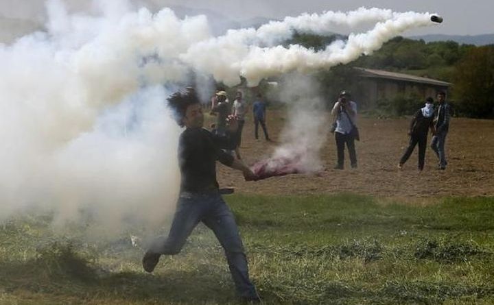 Un imigrant aruncă înapoi o grenadă cu gaz lacrimogen în timpul ciocnirilor cu poliţia macedoneană la graniţa dintre Grecia şi Macedonia, în apropiere de satul elen Idomeni, 13 aprilie 2016.