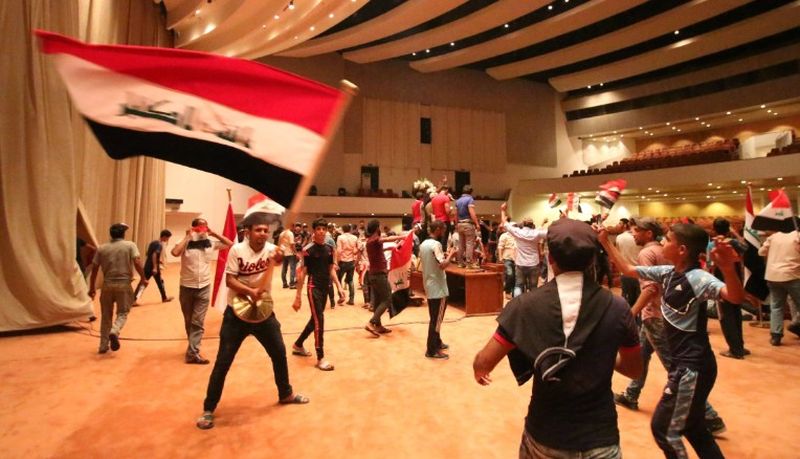 Manifestanţi irakieni flutură steagul naţional în interiorul clădirii Parlamentului după ce au pătruns în Zona Verde puternic fortificată din Bagdad, 30 aprilie 2016.
