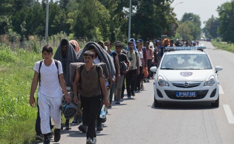 Imigranţi şi refugiaţi mărşăluiesc pe un drum în Indjija, fiind escortaţi de un vehicul al poliţiei, aproximativ 40 km nord-vest de Belgrad, Serbia, 23 iulie 2016. (Captură Foto)