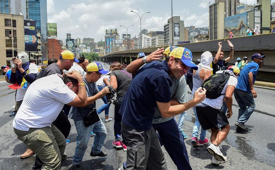 Liderul opoziţiei venezuelene Henrique Capriles se protejează de gazele lacrimogene lansate de forţele de securitate în timpul unui protest anti-guvern în luna aprilie în Caracas. Luni, 29 mai 2017, în cadrul unui alt protest anti-guvern în capitala Venezuelei, Capriles a fost bătut de membri ai Gărzii Naţionale.