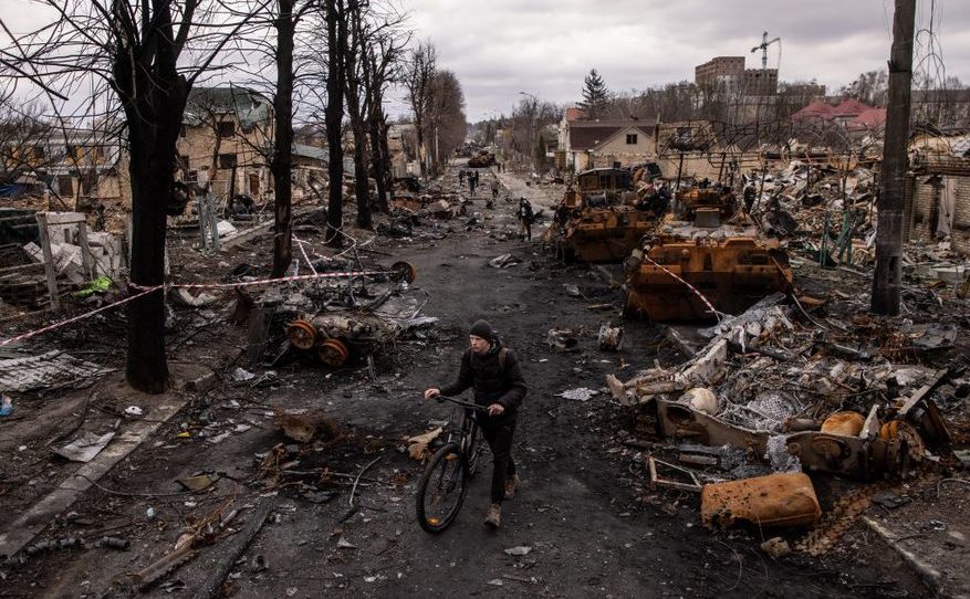 Un bărbat merge pe lângă bicicleta sa printre dărâmături şi vehicule militare ruseşti distruse în oraşul ucrainean Bucea, 6 aprilie 2022