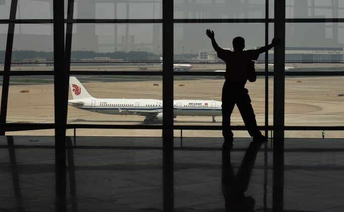 Un bărbat se uită la un avion prin fereastra aeroportului internaţional din Beijing.