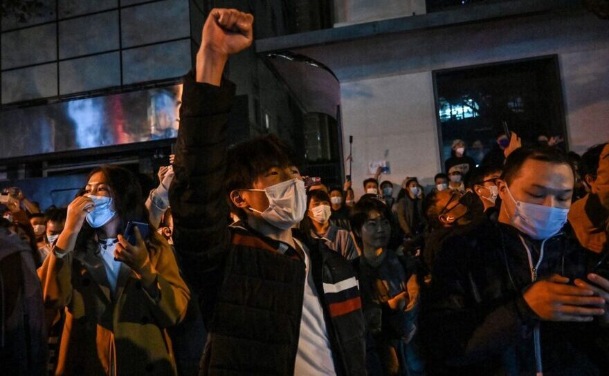Oamenii cântă sloganuri în timp ce protestează pe o stradă din Shanghai, 27 noiembrie 2022.