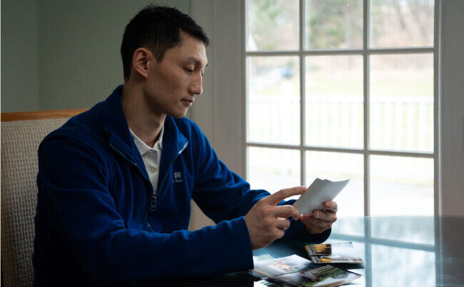 Steven Wang, dansator principal al Shen Yun, se uită la fotografii de familie în casa sa din statul New York, pe 31 martie 2023. (Samira Bouaou/The Epoch Times)