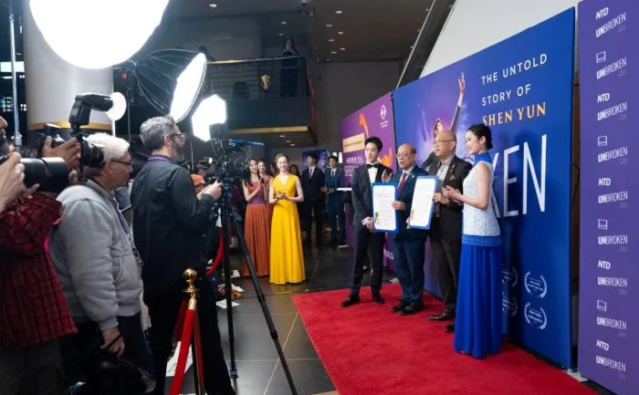 Consilierul municipal din New York, Phil Wong (al doilea din stânga), şi şeful serviciilor pentru cetăţeni, Bernard Chow (al doilea din dreapta), înmânează o proclamaţie Shen Yun Performing Arts alături de dansatorii principali Piotr Huang (stânga) şi Angelia Wang (dreapta), cu ocazia premierei mondiale a spectacolului „Unbroken: The Untold Story of Shen Yun” la AMC Lincoln Square, în New York, pe 24 martie 2026. (Samira Bouaou/Epoch Times)